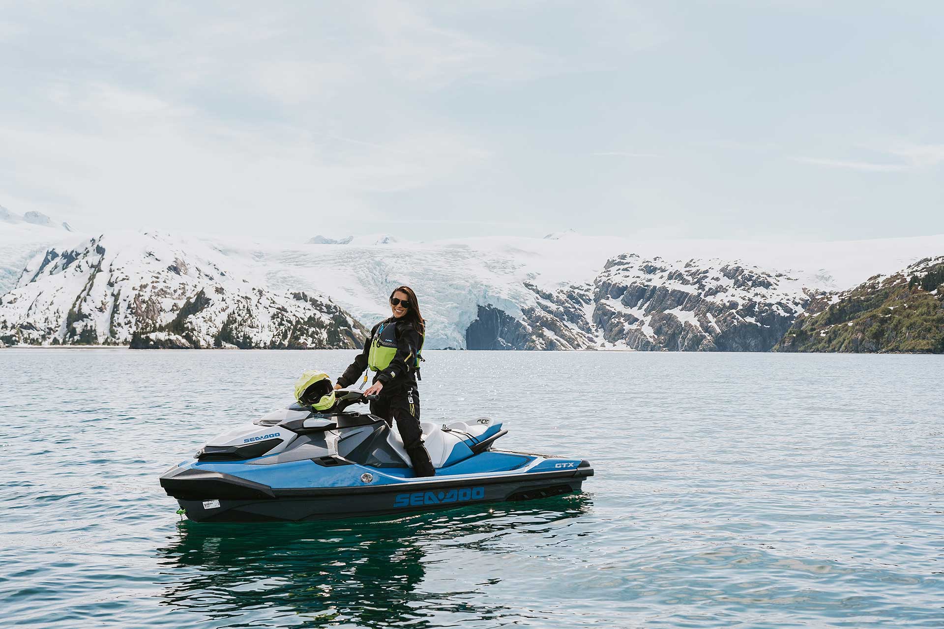 Smiling Young Woman Standing on Jetski in front of Large Glacier