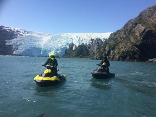 Jet skiers bob on the water in front of a huge glacier