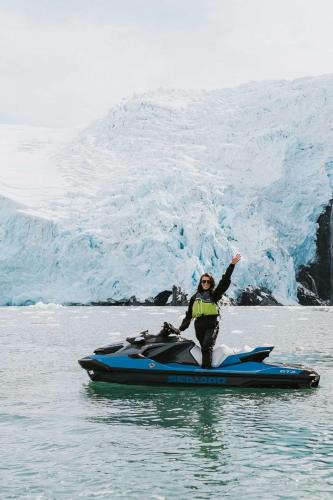 Smiling Woman Posing on Jetski in front of Large Glacier Covered in Snow