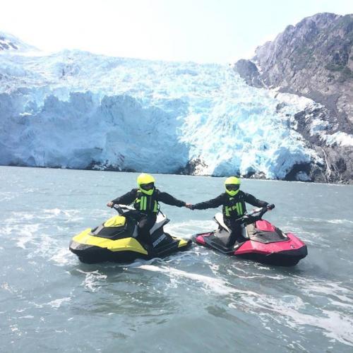 Two jet skiers pose in front of a glacier on a jet ski tour